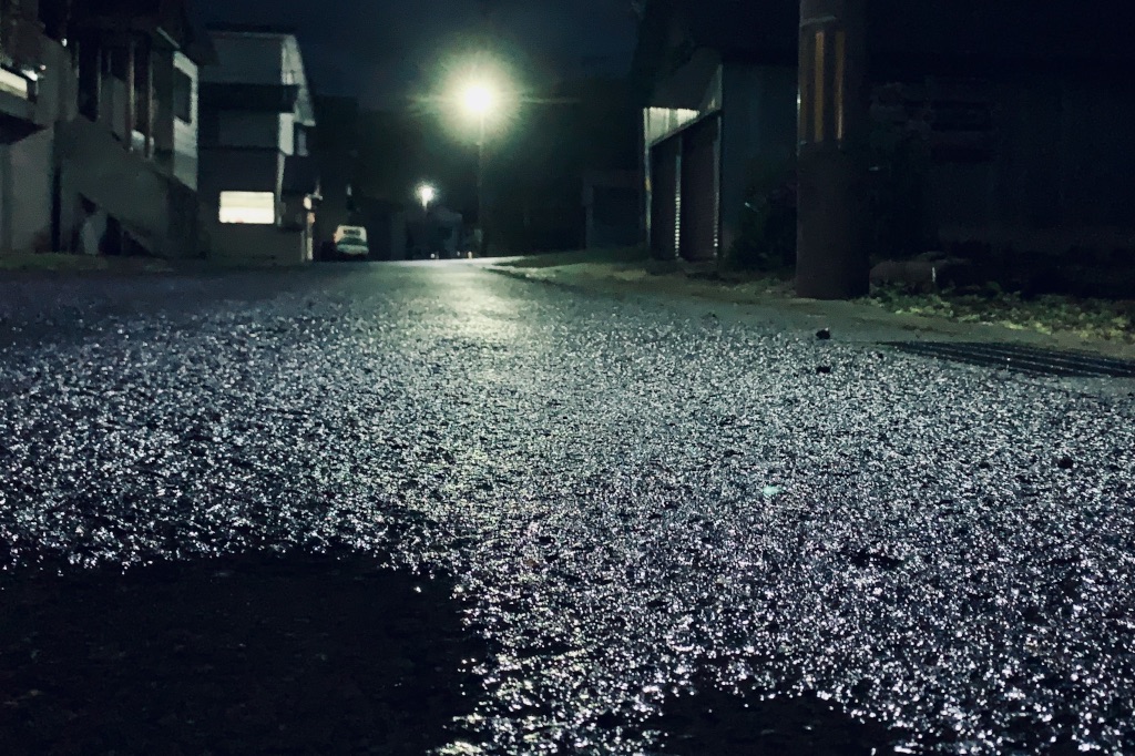 Lamppost shining on road at night after rain.